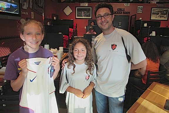 Sarah Margaret Veres, along with Anna Rene Lewis and Mitch Singleton, shows off the U.S. World Cup jersey she won during Monday's kickoff party at Batter Up.