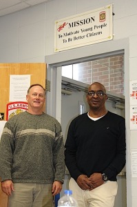 Maj. Don Drummond, left, and 1SG Pringle under the mission statement sign of the DHS JROTC program.