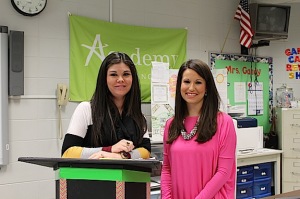 Kelly Gandy (L) and Courtney Kerby standing before the Academy of Finance banner and a culmination project by student Mya Smith. 