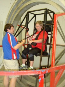 Andrea Clanahan prepares to ride the simulator as a Space Academy instructor buckles her in.