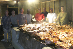 The meat for Jefferson Volunteer Fire Department's barbecue is cooked over a bed of hickory coals all day and all night by members of the department. Pictured left to right are Buddy Lindsay, Chief George Norris, Tom Whitaker, Bobby Lynch, Tim Day, Assistant Chief Joe Coats, Brent King, and Dave Compton.